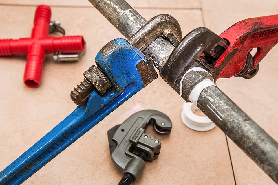 blue and red wrenches are visible working on a pipe in a commercial plumbing setting